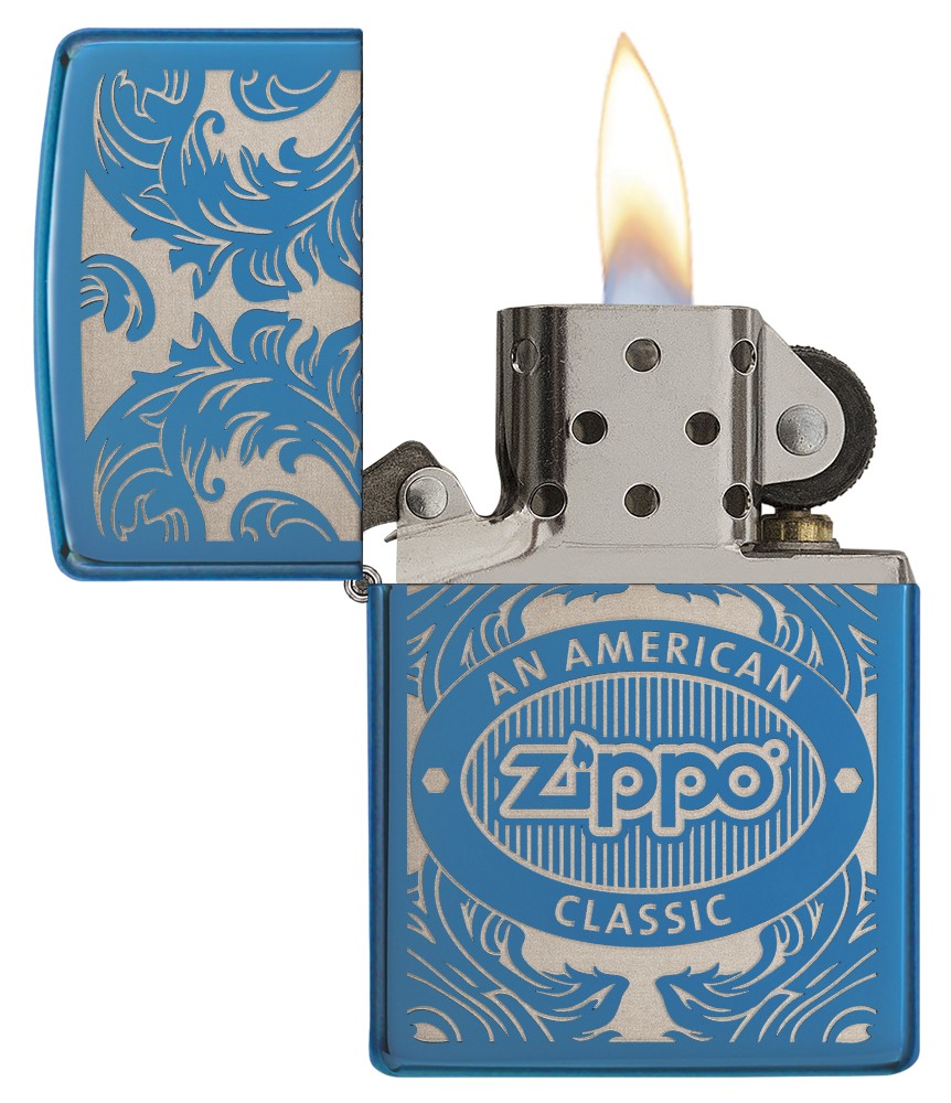 Open front view blue Zippo lighter with flame surrounded by a laser-engraved filigree motif showing the Zippo logo and "an american classic".