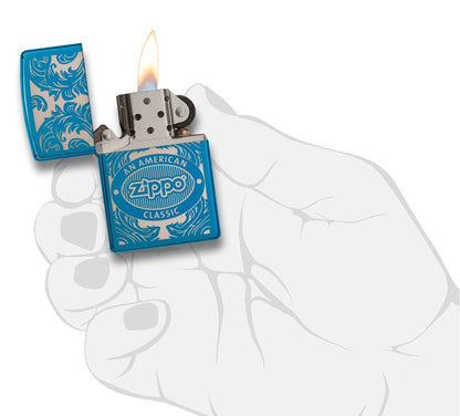 Blue Zippo lighter seen from the front in a stylised open hand with flame surrounded by a laser-engraved filigree motif showing the Zippo logo and "an american classic".