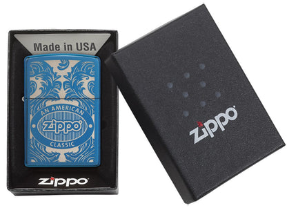 Blue Zippo lighter seen from the front in an open black gift box surrounded by a laser-engraved filigree motif showing the Zippo logo and "an american classic".